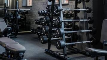 Un gimnasio con equipamiento de levantamiento de pesas, bancos y una pared de ladrillo de fondo.