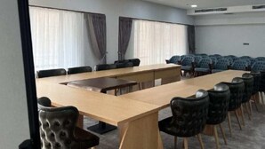 Una sala de conferències amb una taula llarga, diverses cadires i cortines a les finestres.