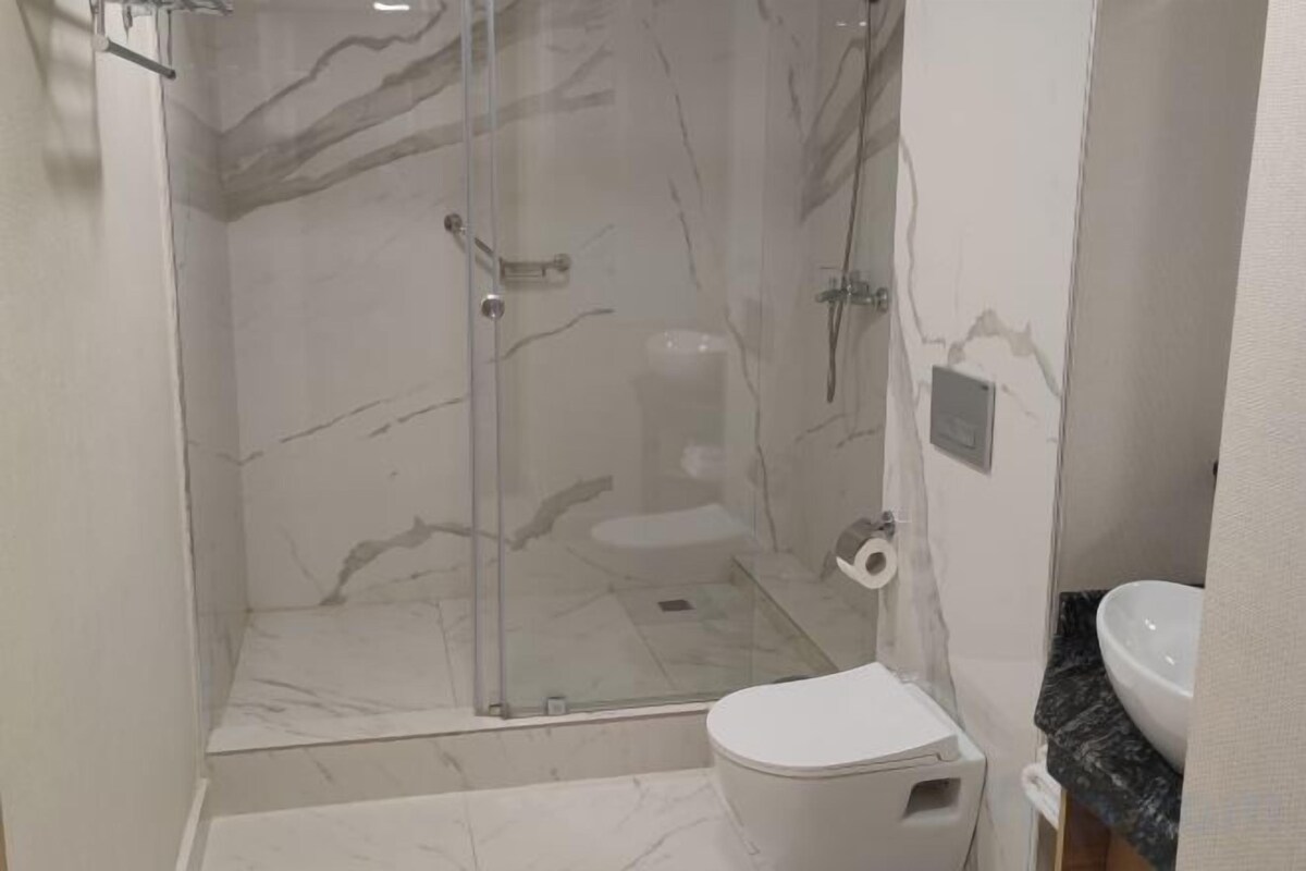 A bathroom with a glass-enclosed shower, a toilet, and a sink.