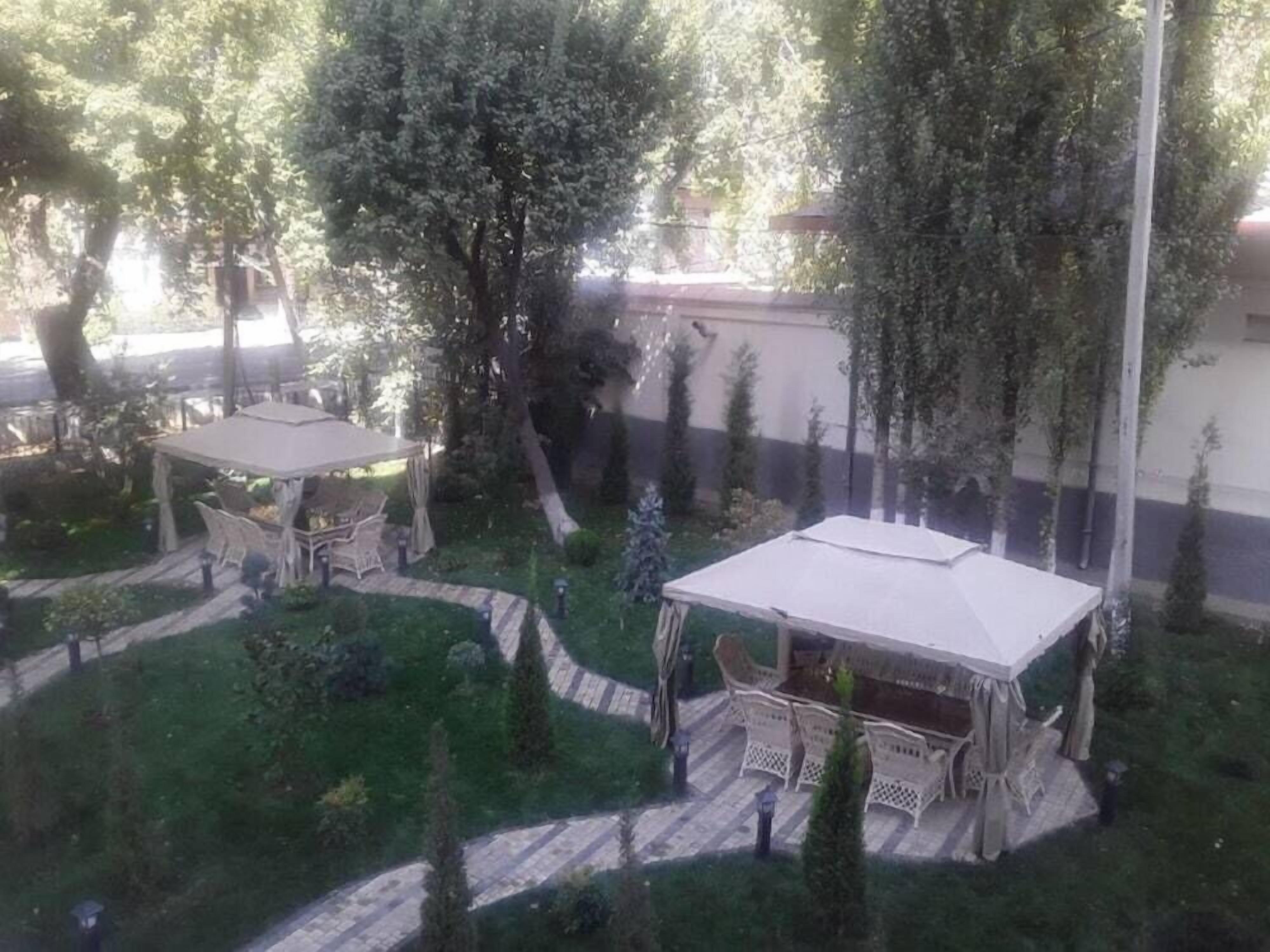 A garden with two outdoor seating areas, surrounded by trees and a pathway.