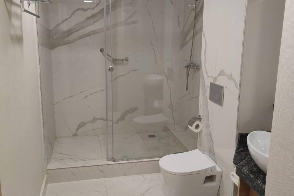 A bathroom with a glass-enclosed shower, a toilet, and a sink with a marble countertop.
