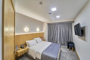 A hotel room with a bed, bedside table, lamp, curtains, and a TV mounted on the wall. - Asli Makon Hotel (Tashkent)