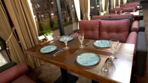 Un restaurant amb una taula de menjador llarga, seients acolchits i grans finestres.