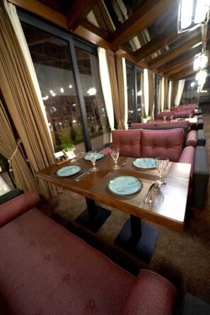 A restaurant with a long dining table, cushioned booths, and large windows. - Asli Makon Hotel (Tashkent)