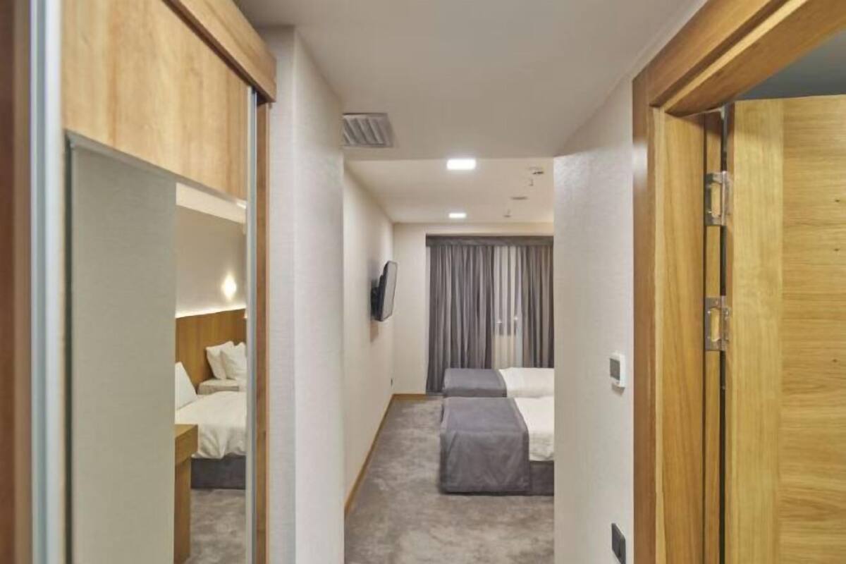 A narrow hallway leading to a bedroom with a bed, a bedside table, and a television mounted on the wall.