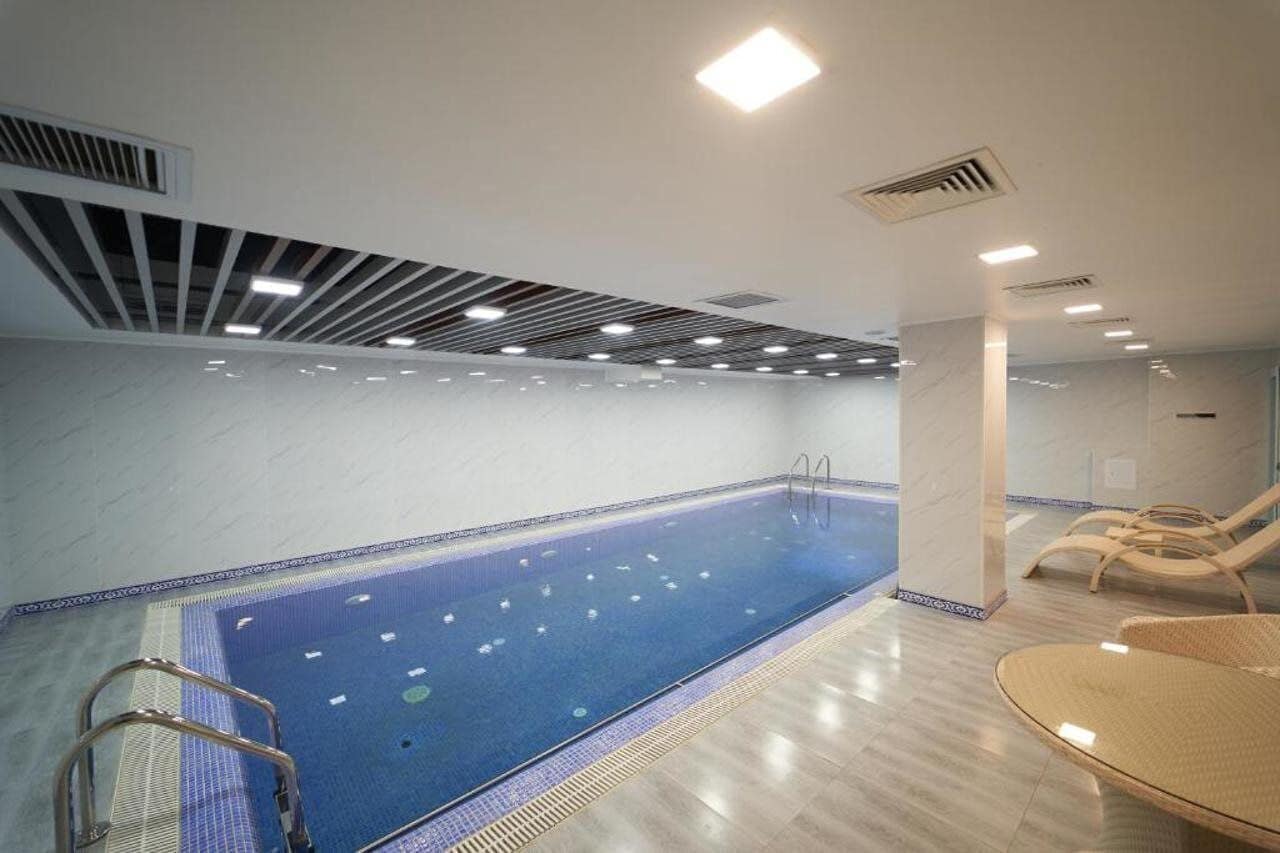 A swimming pool with a tiled floor, a ladder, and lounge chairs.