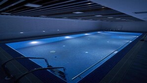 Una piscina interior amb una superfície d'aigua nítida, envoltada de parets i un sostre amb un dibuix de reixa.