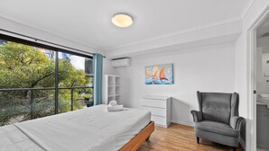 A modern bedroom with a large bed, a grey armchair, a white dresser, and a painting on the wall. - Central Bowen Hills Stay (Brisbane)