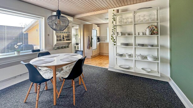 A modern kitchen with a dining area, featuring a round table with chairs, a hanging light fixture, and a white shelving unit with dishes. - 2 bedroom gorgeous home in østermarie (Østermarie)