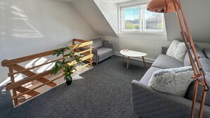A cozy loft bedroom with a sloped ceiling, a grey sofa, a small white table, and a wooden ladder. - 2 bedroom gorgeous home in østermarie (Østermarie)