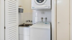 A compact laundry room with a washing machine, a sink, and a drying rack. - Oceanfront 3-bed Retreat With Pool-steps to Beach (Sunshine Coast)