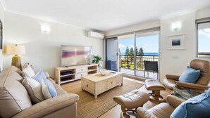 A modern living room with a sofa, coffee table, and TV. There is a balcony with a view of the sea. - Oceanfront 3-bed Retreat With Pool-steps to Beach (Sunshine Coast)
