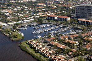 An aerial view of a marina with boats, a residential area with uniform architecture, and a large building in the background.