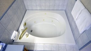 A bathroom with a white bathtub, a towel rack, and a small trash bin. - 1 King Bed Jetted Tub (Fresno)