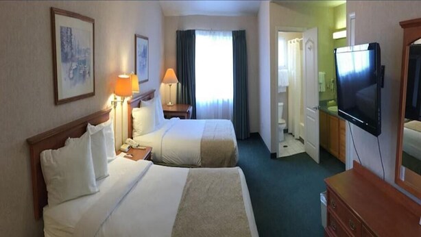 Een hotelkamer met twee bedden, een televisie, een dressoir en een badkamer door een geopende deur.
