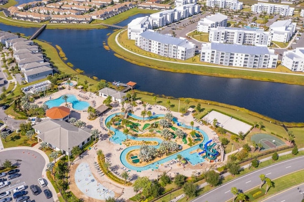 An aerial view of a resort with a central swimming pool, a water park, and adjacent residential buildings.