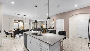 A modern kitchen with a central island, pendant lighting, and a dining area with chairs and a table. - DisneyVilla 6 BD, Club/Water Park/Pool/Spa and BBQ (Kissimmee)