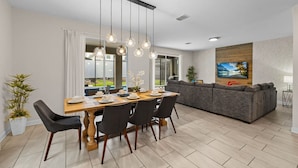 A modern living room with a sofa, a dining area with a table set for four, and a TV mounted on the wall. - DisneyVilla 6 BD, Club/Water Park/Pool/Spa and BBQ (Kissimmee)