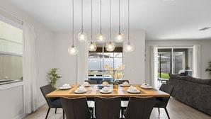 A dining area with a wooden table set for six, surrounded by chairs, with a modern pendant light fixture above. - DisneyVilla 6 BD, Club/Water Park/Pool/Spa and BBQ (Kissimmee)