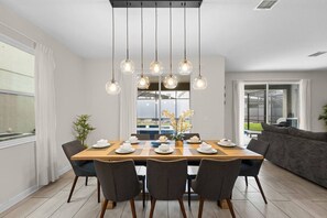 A dining area with a wooden table set for six, surrounded by chairs, with a modern pendant light fixture above.