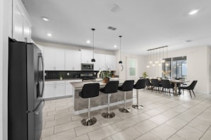A modern kitchen with white cabinets, a black refrigerator, and a bar area with black bar stools.