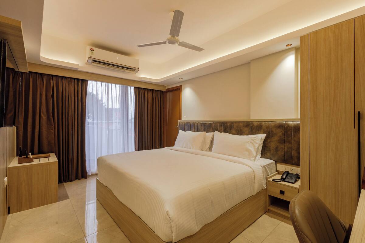 A hotel room with a large bed, a desk, a chair, a wardrobe, and a ceiling fan.
