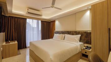 A hotel room with a large bed, a desk, a chair, a wardrobe, and a ceiling fan.