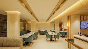 Un ristorante moderno con un lungo bancone, diversi tavoli e sedie imbottite verdi.