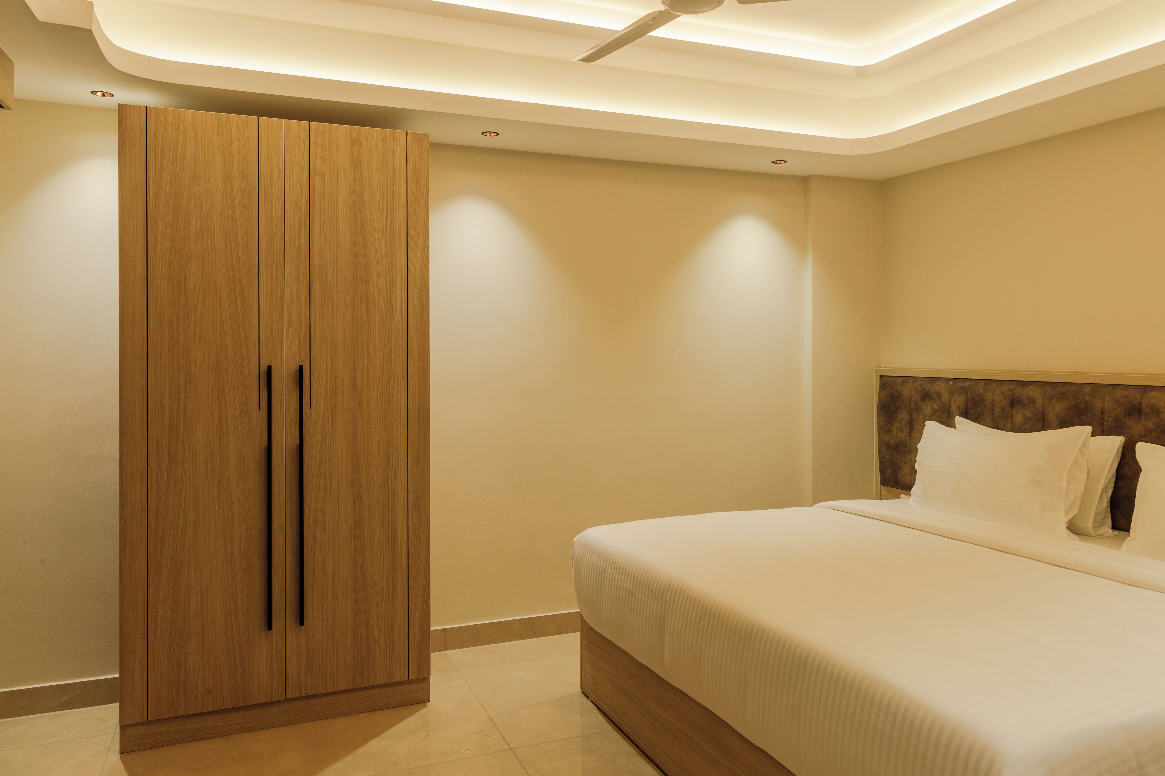 A bedroom with a large wardrobe, a bed with white linens, and a ceiling fan.