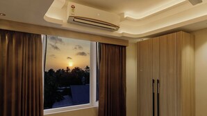 Una stanza con una grande finestra, tende marroni, condizionatore d'aria a soffitto e mobili in legno.