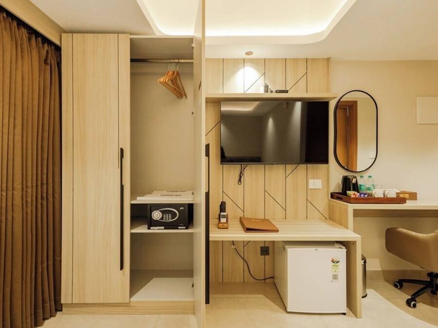 Une chambre d’hôtel compacte comprenant une armoire en bois, un petit bureau avec une chaise, une télévision et un réfrigérateur.