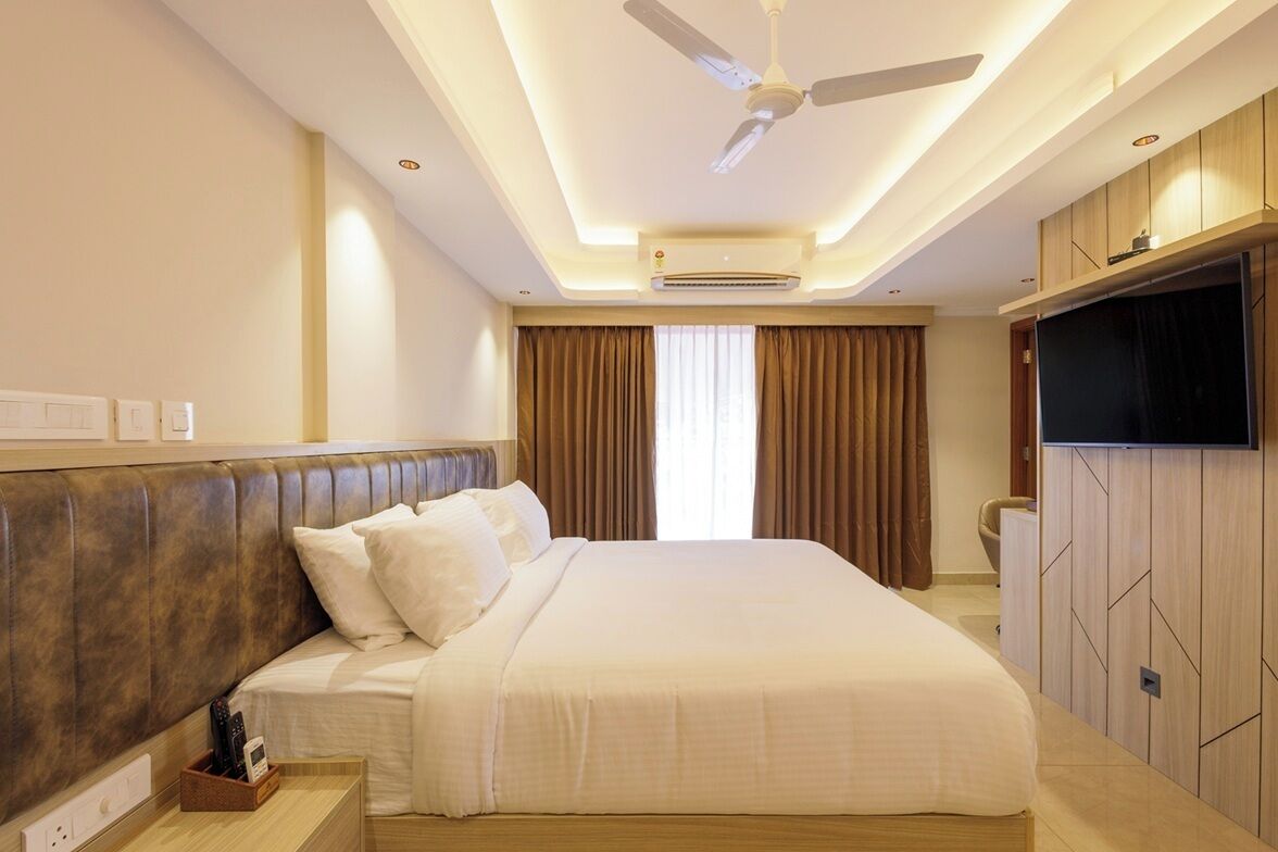 Ein Hotelzimmer mit einem großen Bett, einem Deckenventilator, einer Klimaanlage, einem an der Wand montierten Fernseher und einem Fenster mit Vorhängen.