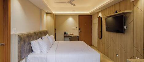 A modern hotel room with a large bed, a desk, a flat-screen TV mounted on the wall, and a ceiling fan.