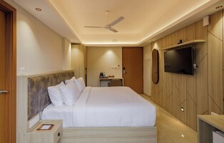 A modern hotel room with a large bed, a desk, a flat-screen TV mounted on the wall, and a ceiling fan.
