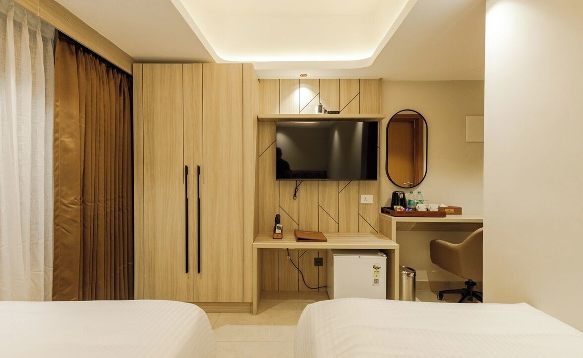 A hotel room with two beds, a desk with a TV, a mirror, and a small fridge.