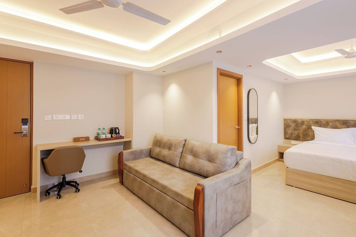 A modern hotel room with a sofa, a desk, a chair, a bed, and a ceiling fan.
