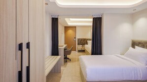 Una moderna camera d'albergo con un letto, una scrivania, una sedia e un bagno parzialmente visibile attraverso una porta aperta.