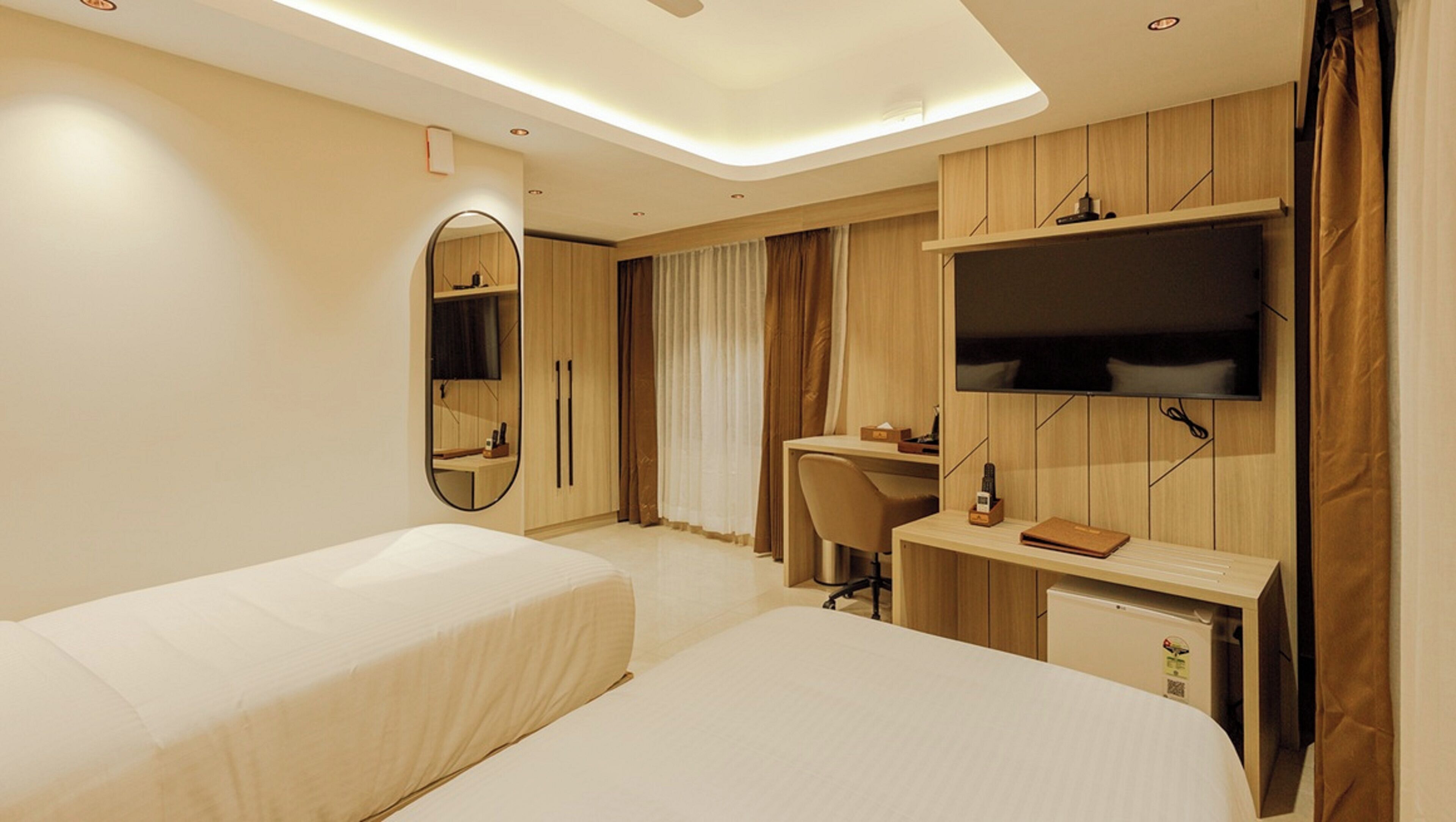 A hotel room with two beds, a desk, a chair, a TV, and a wardrobe.