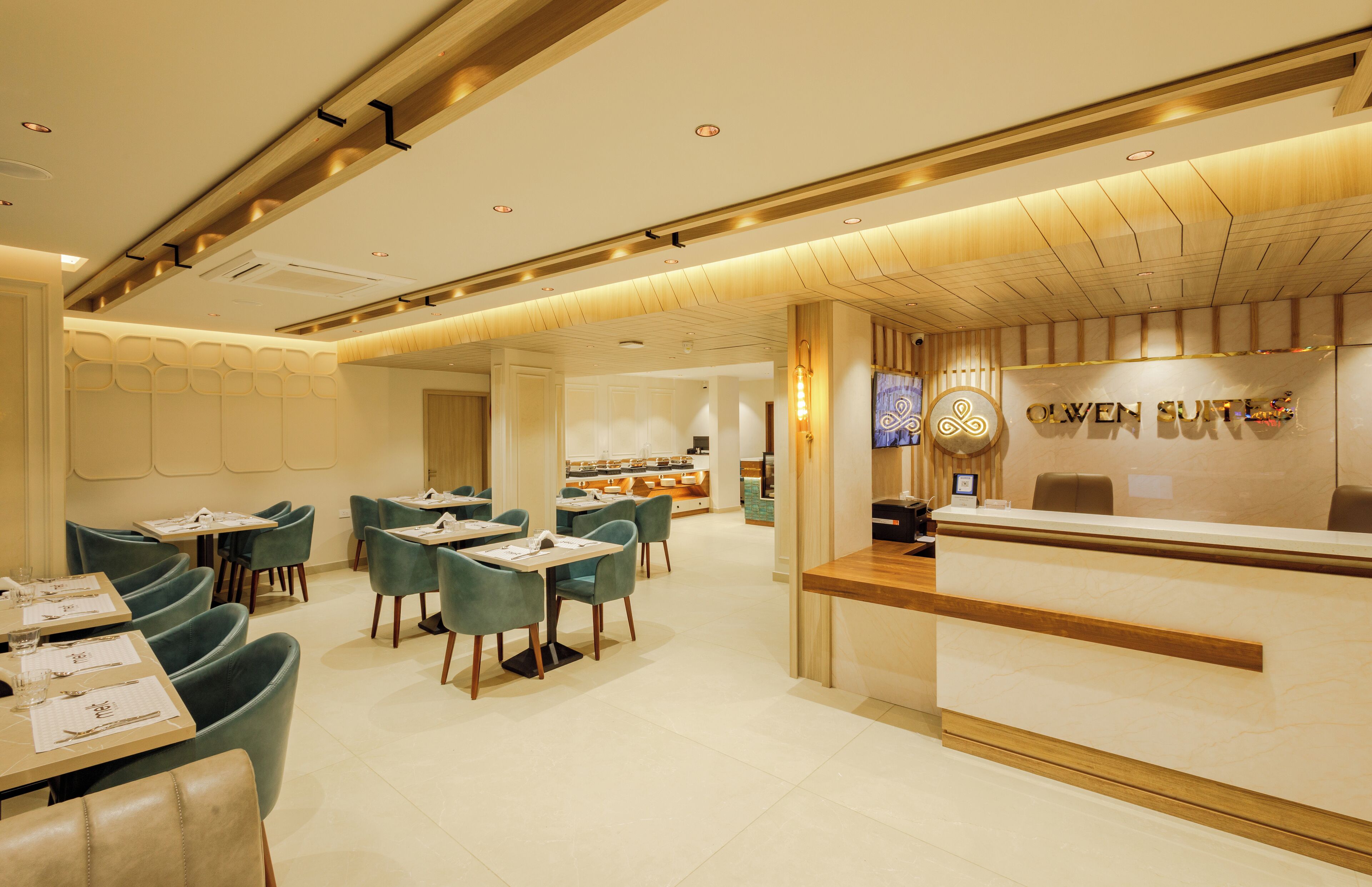 A modern hotel lobby with a reception desk, seating area, and a glimpse of the dining area.