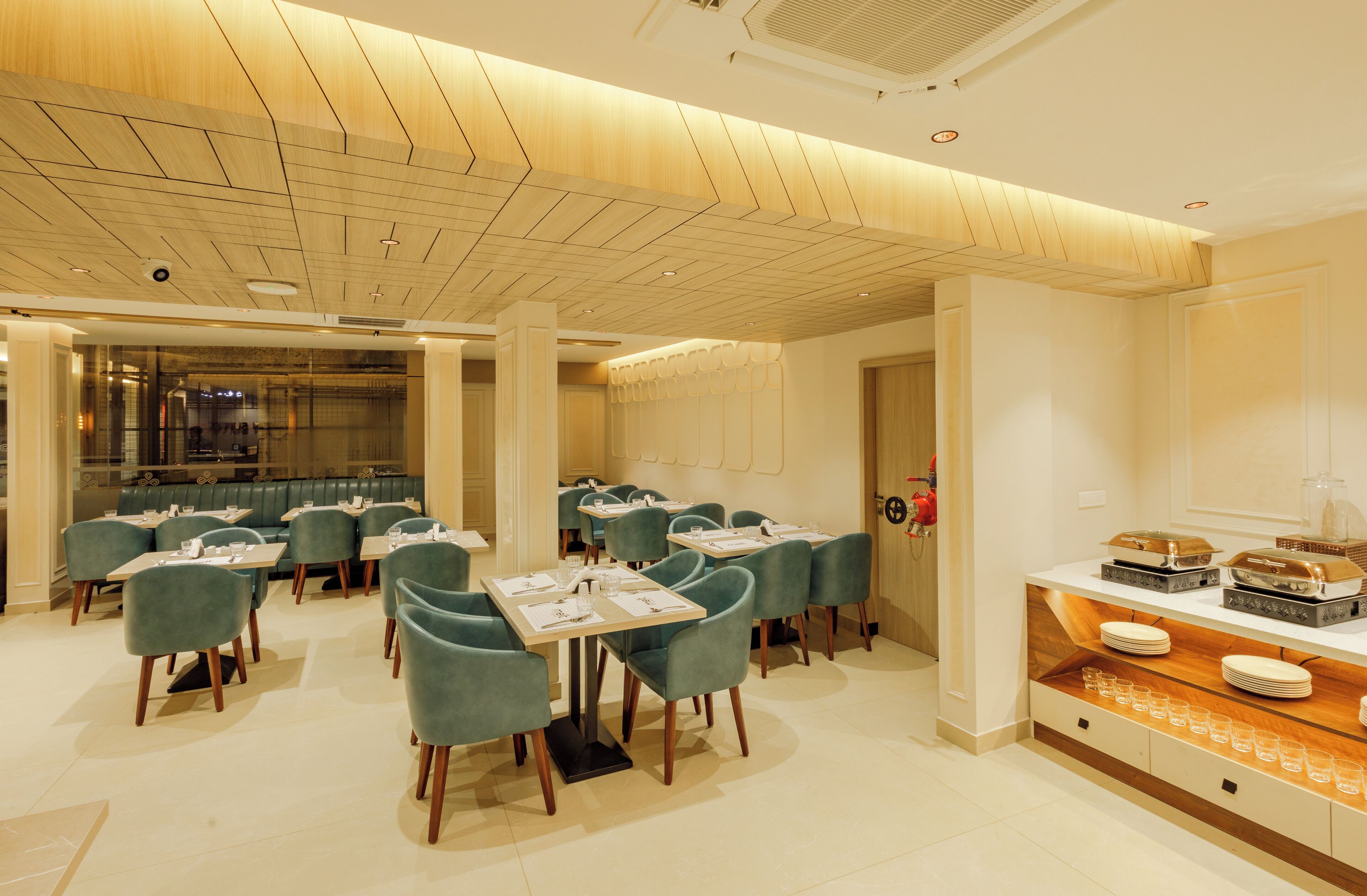 A modern dining area with multiple tables and chairs, a buffet counter, and a kitchen in the background.
