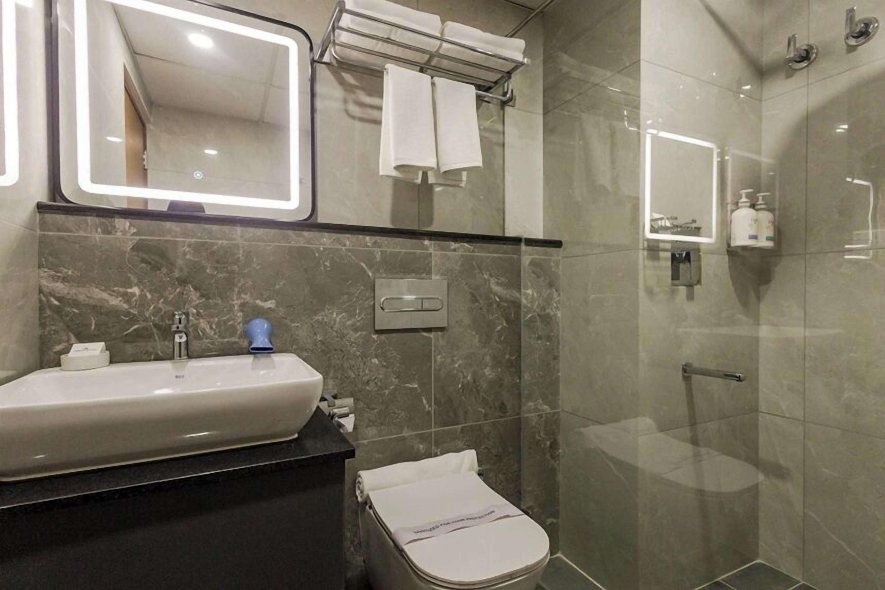A modern bathroom with a marble sink, a toilet, a glass shower enclosure, and a towel rack.