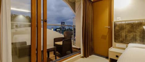 A hotel room with a balcony, a bed, a nightstand, and a view of the cityscape.