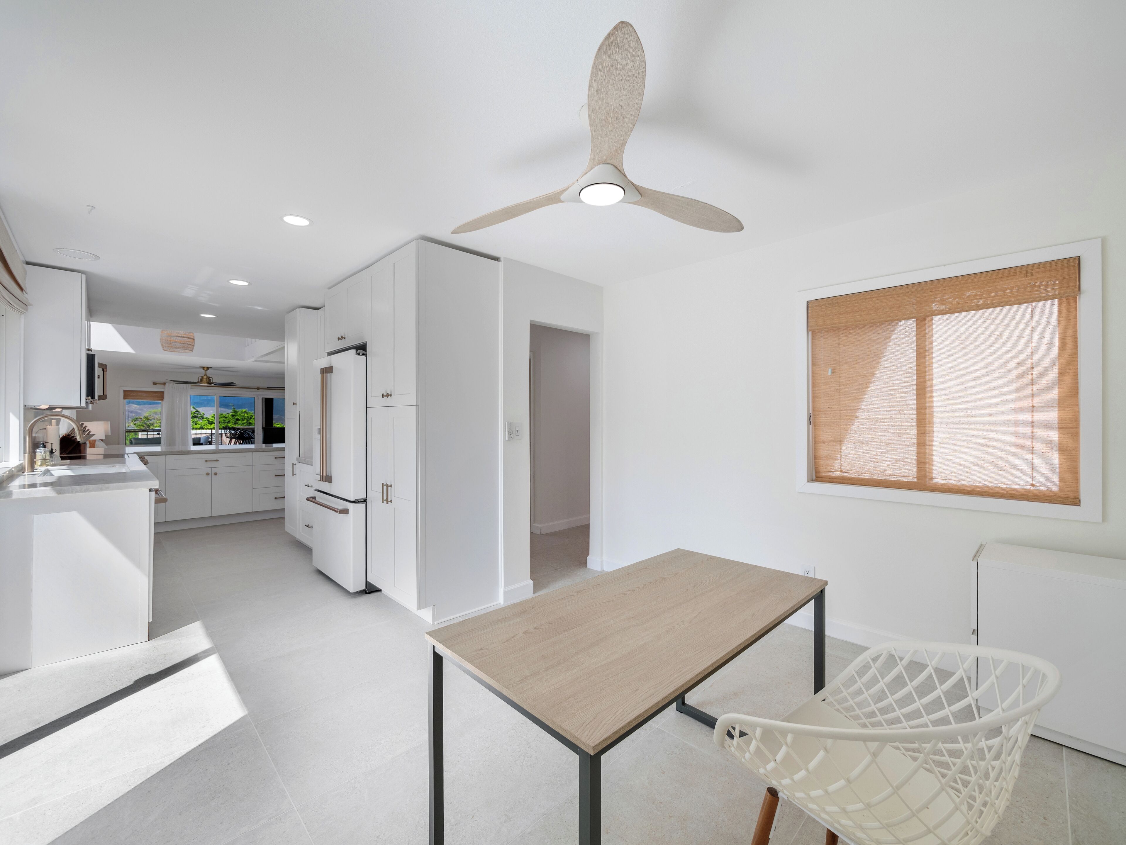 Una cocina moderna con armarios blancos, una mesa de comedor de madera y un ventilador de techo.