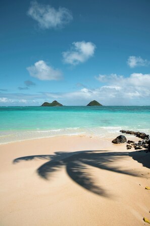 A beach with clear turquoise water, a sandy shore, and two small islands in the distance.