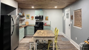A kitchen with a wooden ceiling, a stainless steel refrigerator, a microwave, and a stove. There are yellow chairs and a wooden table.