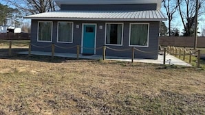 A small, single-story building with a metal roof, a turquoise door, and a chain-link fence in front.