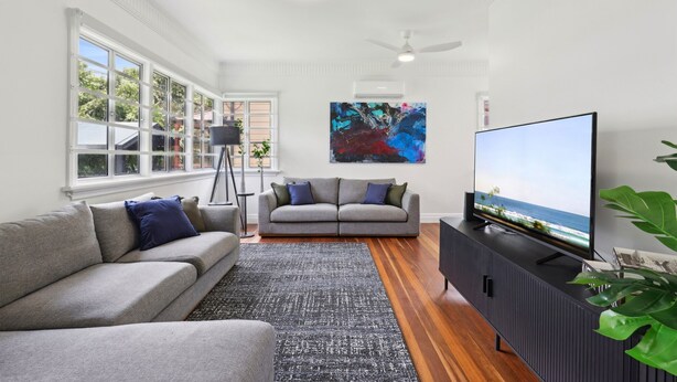 Una sala moderna con un sofá gris, un mueble de entretenimiento negro y un televisor grande mostrando un paisaje.