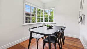 Un comedor con una mesa y sillas de madera oscura, un ventanal de varios paneles y una pared blanca.