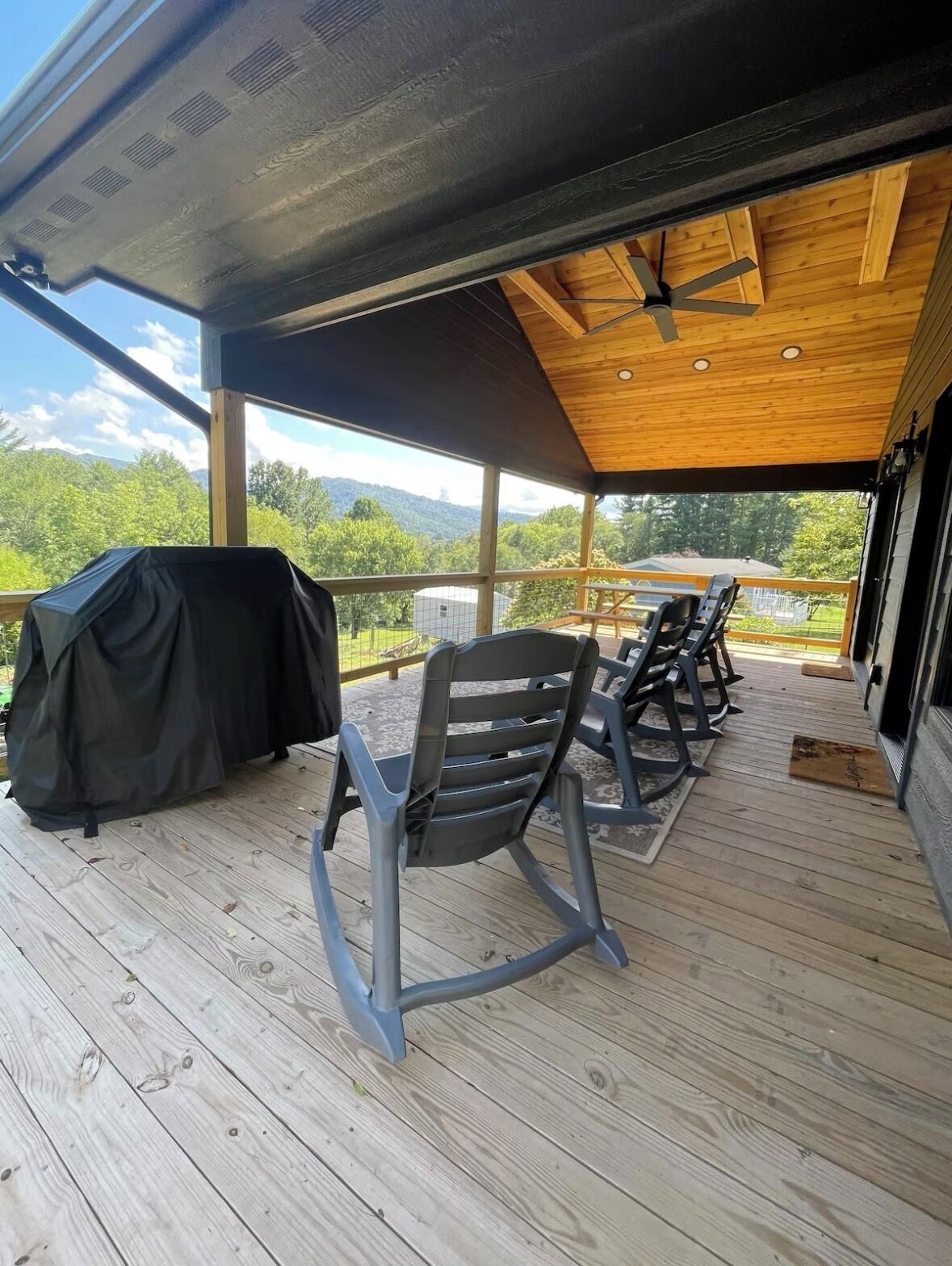 An outdoor deck with wooden flooring, a covered area with a ceiling fan, and a view of a mountainous landscape.