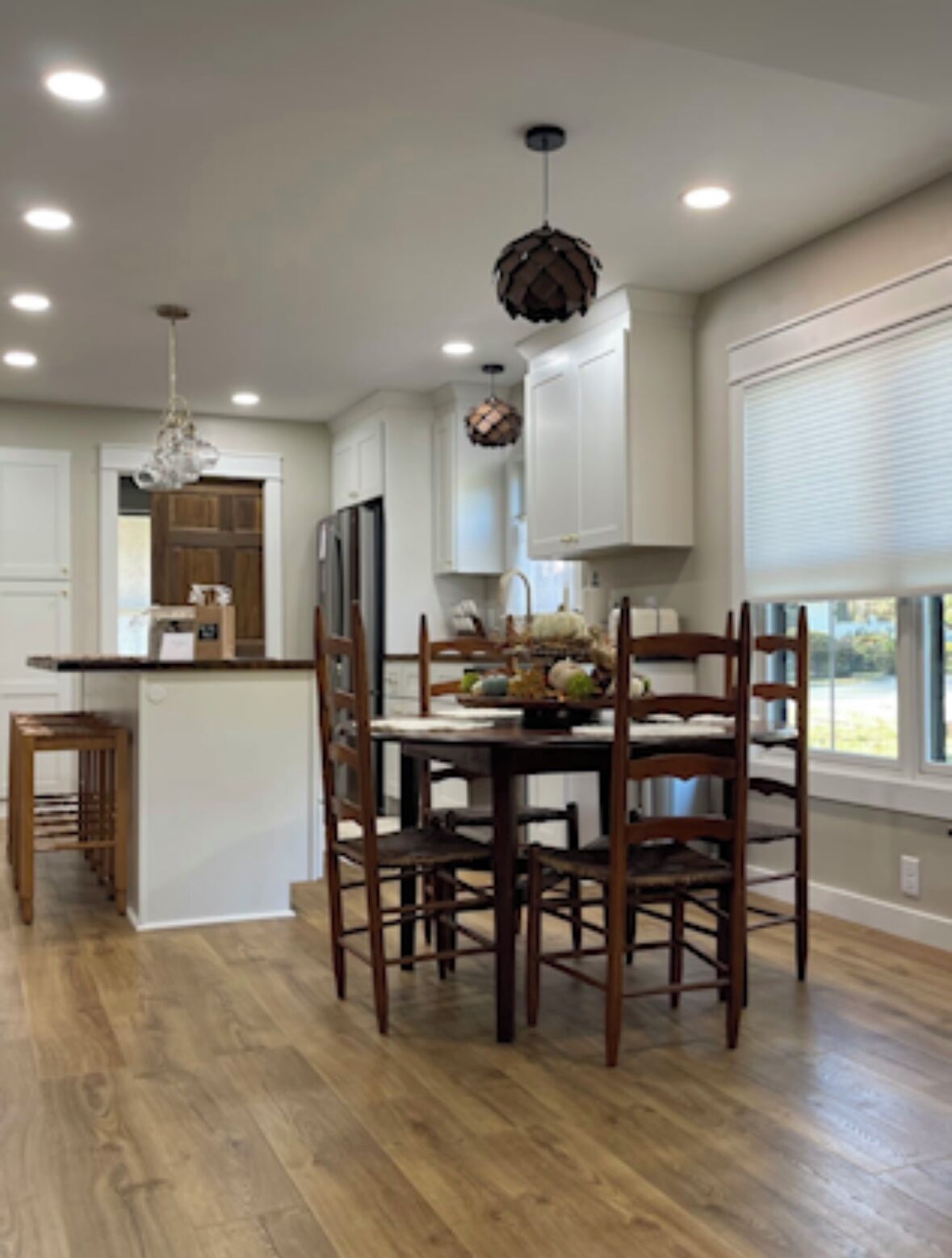 A modern kitchen with white cabinets, a wooden dining table, and a chandelier.